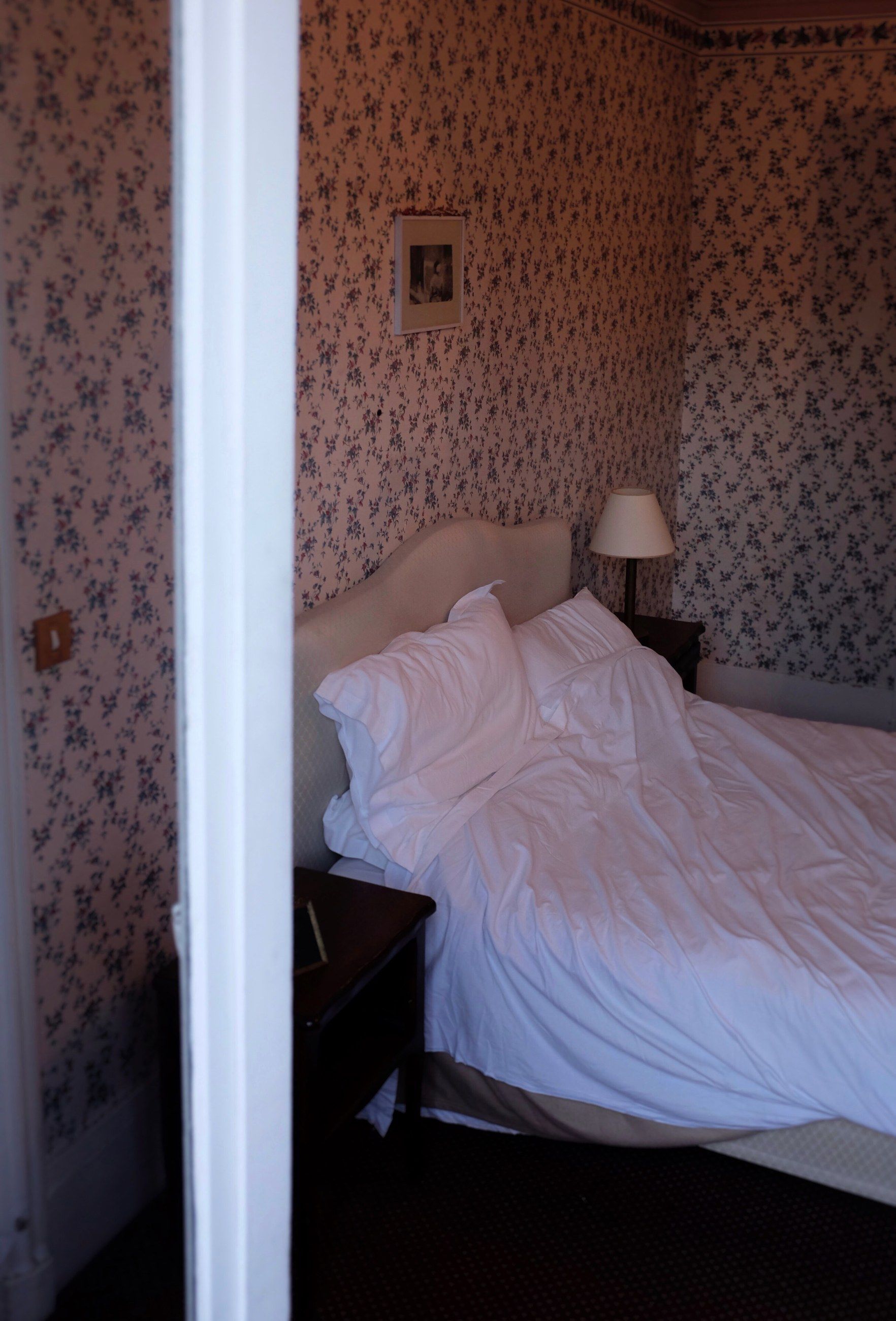 An unmade white bed in a room with patterned wallpaper